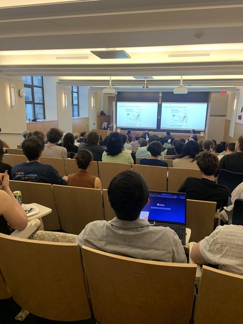View from the back of an auditorium filled with people. At the front of the room, Lisa Margonelli presents as part of a panel discussion.  