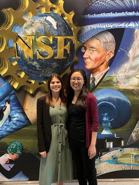 Two women pose in front of a colorful mural with the NSF logo