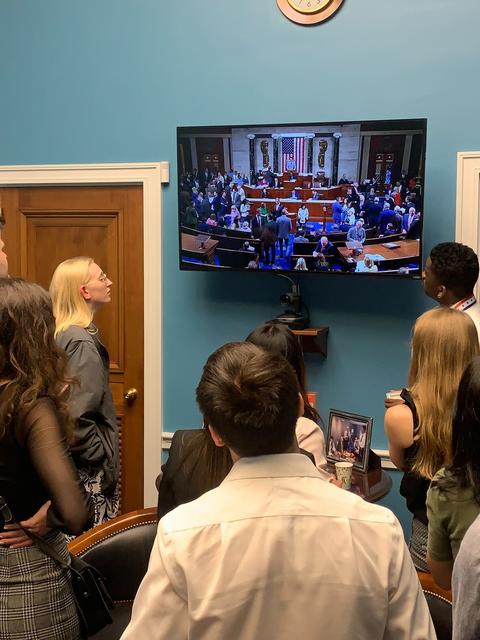 Students watch proceedings on the floor on a TV